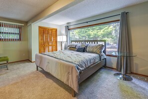Quarto com cama, mesa de cabeceira, abajur, janela com cortinas e vista para árvores.