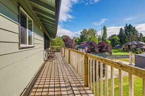 Um deck de madeira com guarda-corpo, uma janela e vista para uma área residencial com casas e árvores.