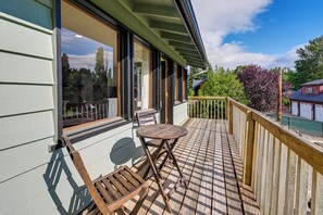 Um deck de madeira com mesa e cadeiras, um corrimão e vista da região ao redor.