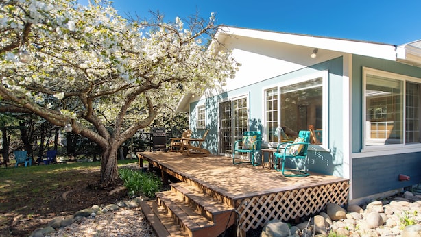 A covered patio with outdoor furniture, a wooden deck, and a view of a house with large windows. - Sequim Escape w/ Gas Grill & Deck, Walk to Beach! (Sequim)