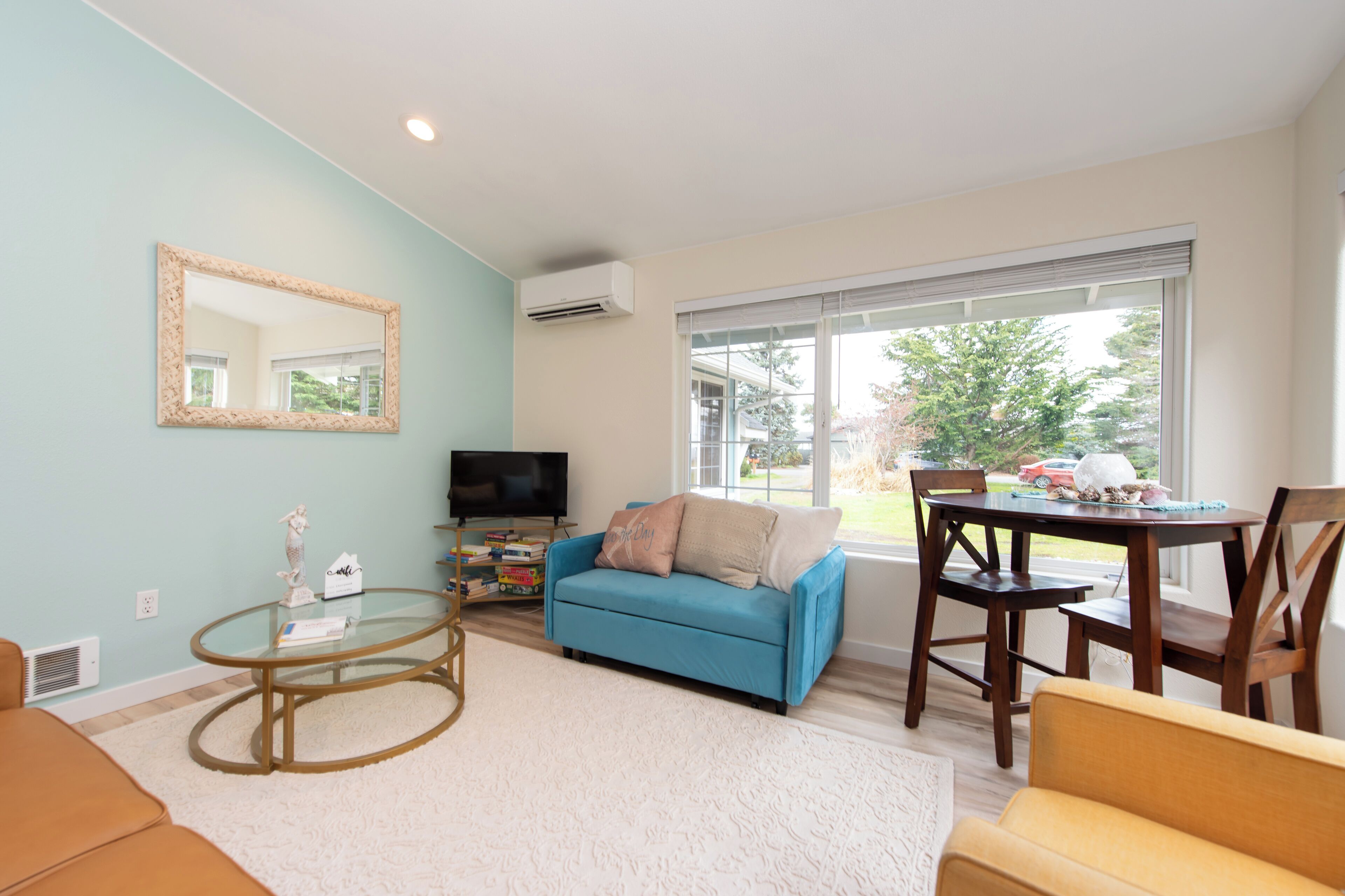 A living room with a blue sofa, a glass coffee table, a TV, and a dining area with a table and chairs.