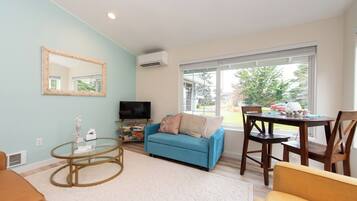 A living room with a blue sofa, a glass coffee table, a TV, and a dining area with a table and chairs.