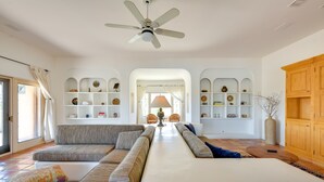 A spacious living room with a large sofa set, a ceiling fan, and built-in shelving with decorative items. - Chic Borrego Springs Home w/ Outdoor Oasis! (Borrego Springs)