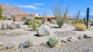 A desert landscape with a building featuring a red facade and arched doorway, surrounded by cacti and rocks. - Chic Borrego Springs Home w/ Outdoor Oasis! (Borrego Springs)