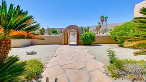 A stone pathway leading to an arched entrance surrounded by desert vegetation and palm trees. - Chic Borrego Springs Home w/ Outdoor Oasis! (Borrego Springs)