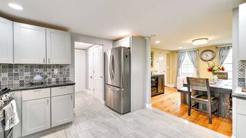 A modern kitchen with white cabinets, a stainless steel refrigerator, and a dining area with a wooden table and chairs.