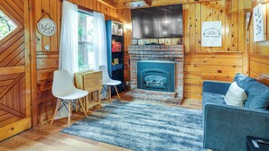 A cozy cabin interior with a fireplace, wooden walls, a sofa, and a dining area. - Fire Pit, Deck & Grill: Cozy Twain Harte Cabin! (Twain Harte)