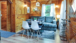 A cozy cabin interior with wooden walls, a dining area with a table and chairs, a sofa, and a small shelf with a sign. - Fire Pit, Deck & Grill: Cozy Twain Harte Cabin! (Twain Harte)
