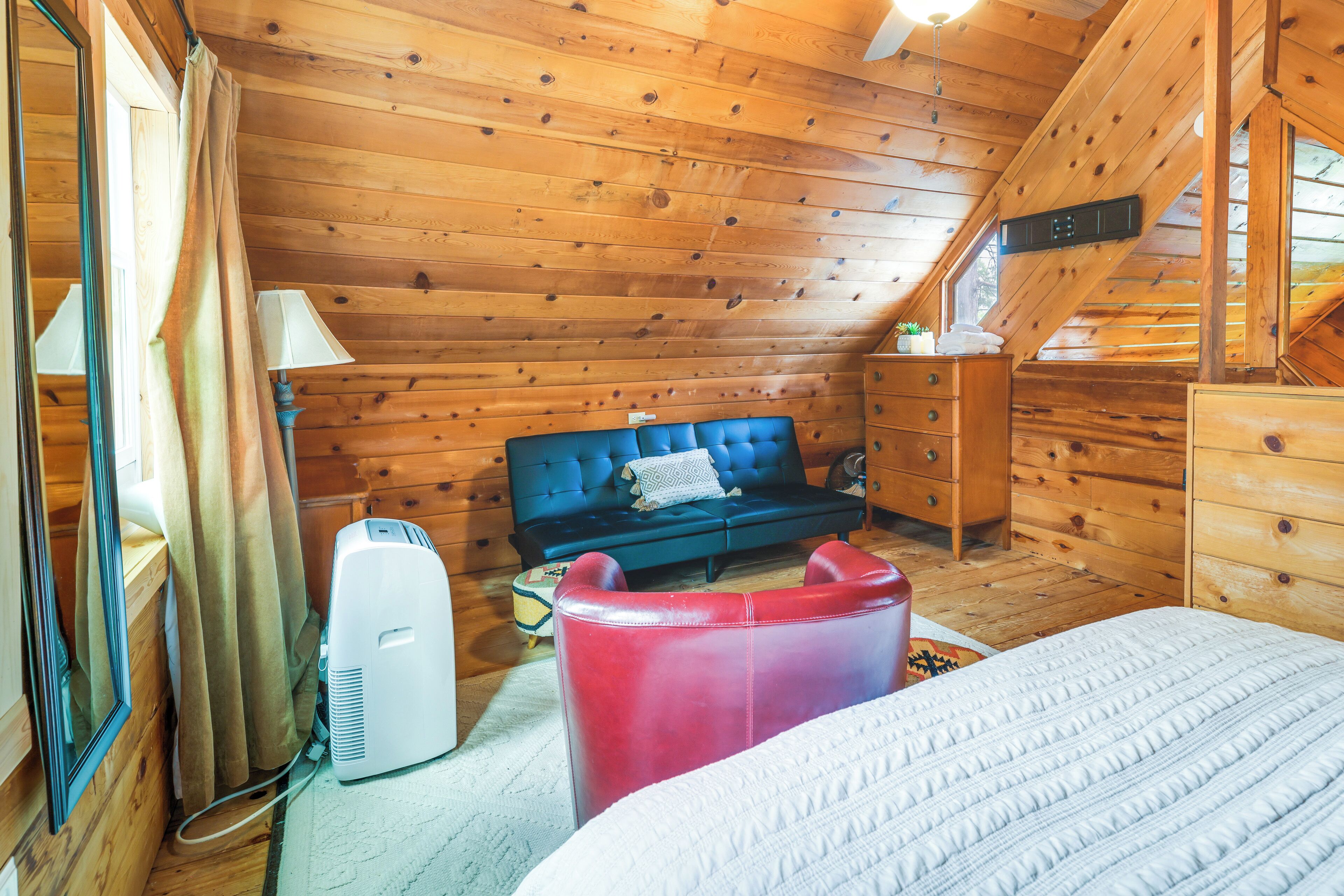 A cozy cabin room with a bed, a blue sofa, a red chair, and wooden walls.
