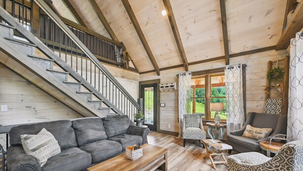Un amplio salón con escalera, pisos de madera y una mezcla de muebles modernos y clásicos.