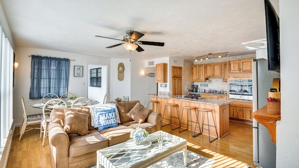 A modern living room with a sofa, coffee table, and dining area. It includes a kitchen with wooden cabinets and a bar area. - Ormond Beach Home: Walk to Community Beach! (Ormond Beach)