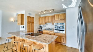 A kitchen with wooden cabinets, a granite countertop, a stainless steel refrigerator, and a built-in oven. - Ormond Beach Home: Walk to Community Beach! (Ormond Beach)
