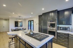 A modern kitchen with dark cabinetry, stainless steel appliances, and a central island with bar stools.