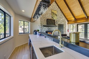A modern kitchen with a large island, stone wall, and wooden ceiling beams. - Lake Views, Game Room, Decks, 3 Ks, 2 Qs, 6 Baths! (Lake Arrowhead)
