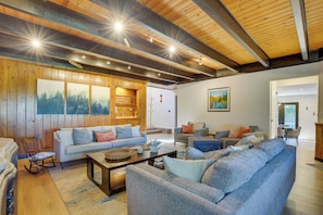 A spacious living room with a wooden ceiling, a large sofa set, a rocking chair, and a dining area.