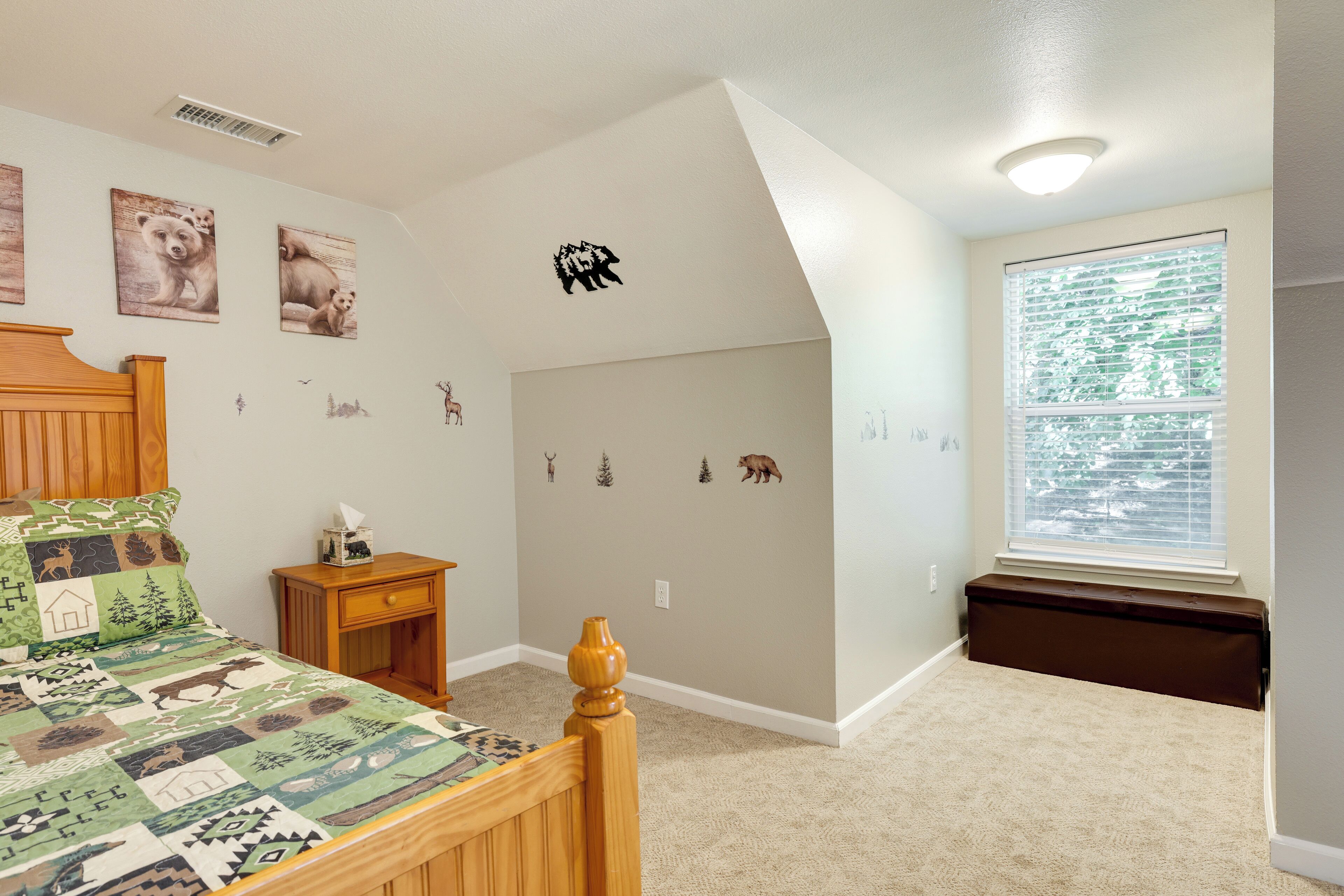 A bedroom with a bed, a nightstand, a window with blinds, and wall decorations including animal stickers.