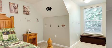 A bedroom with a bed, a nightstand, a window with blinds, and wall decorations including animal stickers.