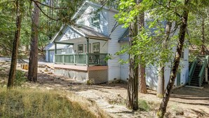 A white house with a green porch and a covered front porch area, surrounded by trees and a dirt path. - Near Dtwn: Twain Harte Home w/ Furnished Deck! (Twain Harte)