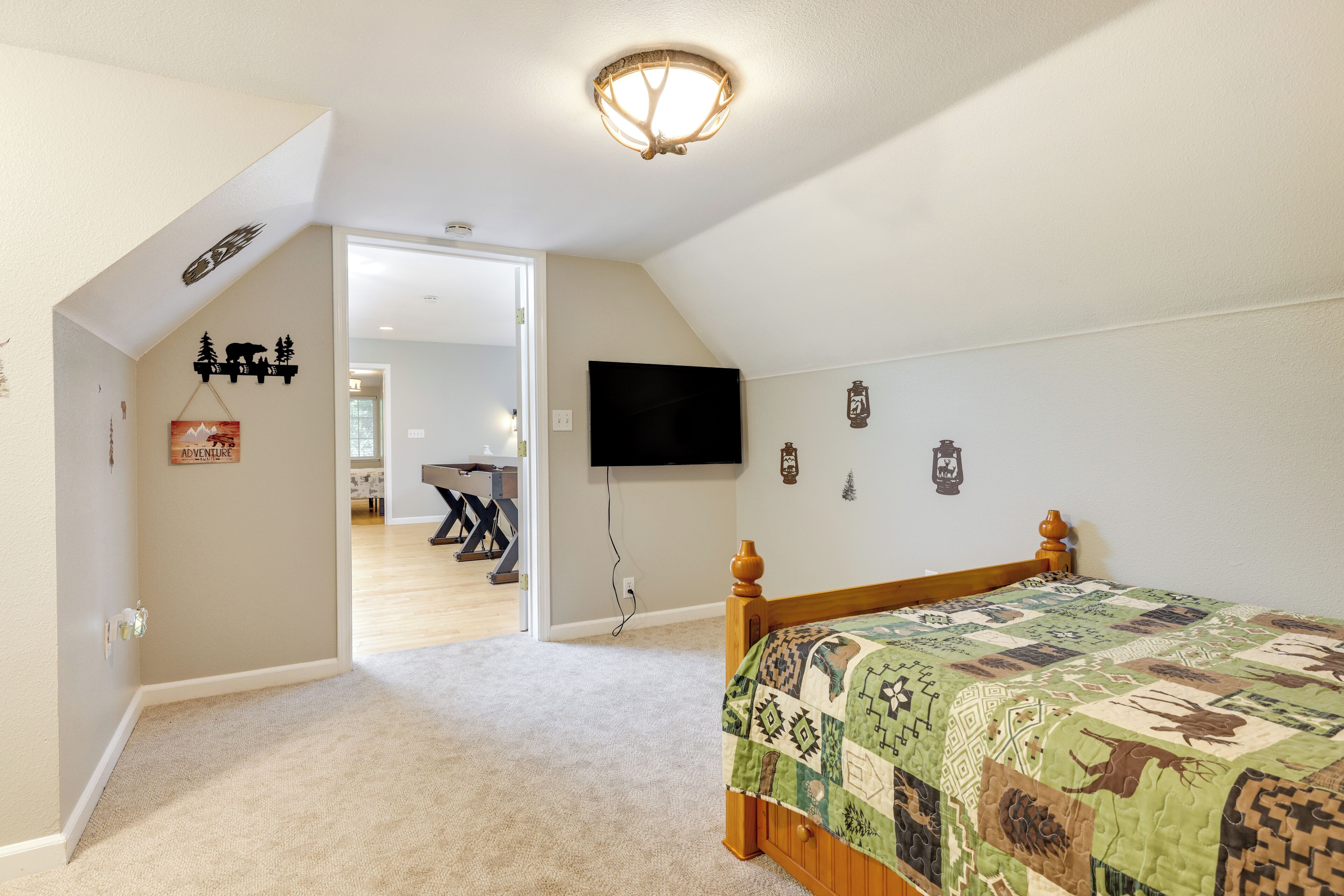 Un dormitorio con una cama grande, una lámpara de techo, un televisor montado y una puerta que da a otra habitación.
