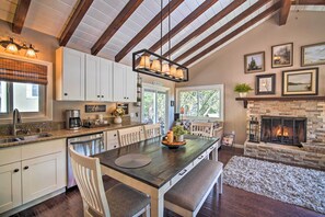 A modern kitchen with white cabinets, a dark wooden island, and a stone fireplace. - Tree-lined Twin Peaks Cottage w/ Custom Stream (Lake Arrowhead)