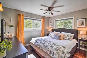 A bedroom with a bed, two bedside tables, a ceiling fan, and windows with curtains. - Tree-lined Twin Peaks Cottage w/ Custom Stream (Lake Arrowhead)