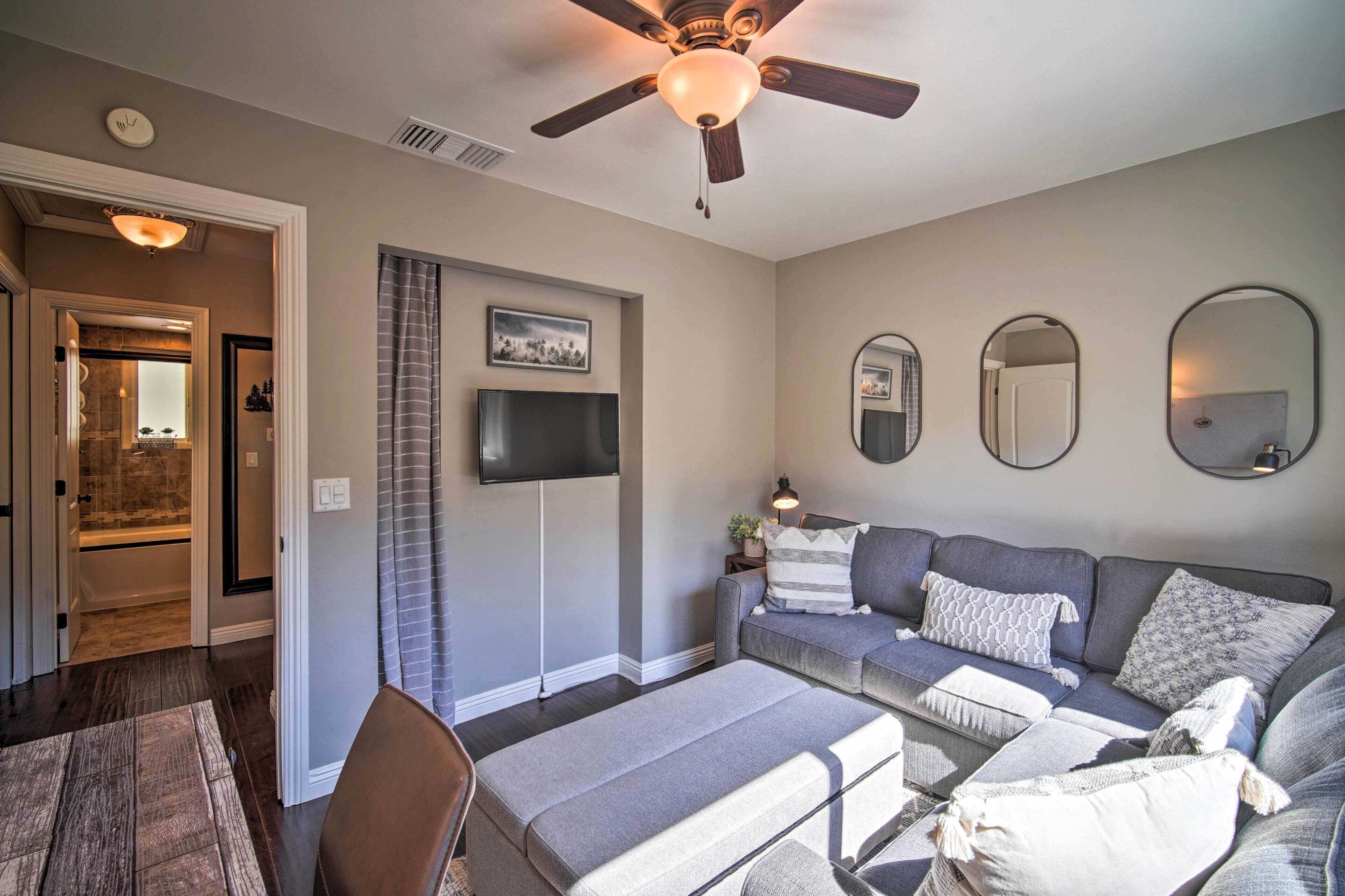 A living room with a grey sofa set, a ceiling fan, a flat-screen TV, and a large mirror.