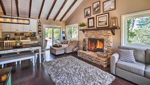 A spacious living area with a fireplace, a dining area with a bench, and a kitchen with white cabinets. - Tree-lined Twin Peaks Cottage w/ Custom Stream (Lake Arrowhead)