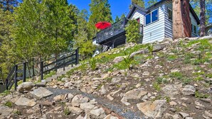 A house with a wooden deck, a red umbrella, and a stone staircase leading up to it. - Tree-lined Twin Peaks Cottage w/ Custom Stream (Lake Arrowhead)