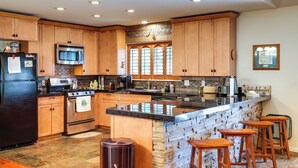 A kitchen with wooden cabinets, a stainless steel refrigerator, a microwave, a stove, and a large island with bar stools. - Cozy Mi-wuk Village Cabin w/ Deck! (Mi-Wuk Village)