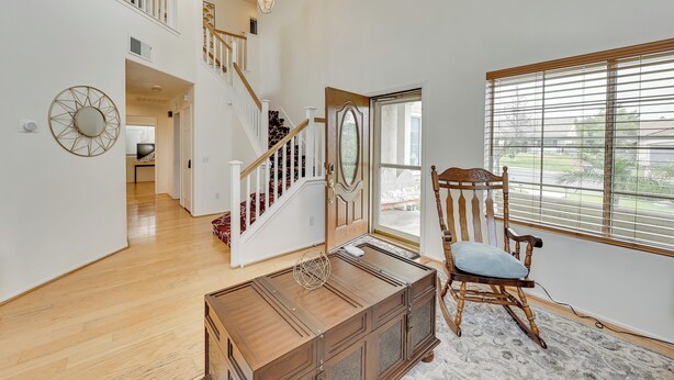 Une pièce spacieuse avec un escalier en bois, une grande fenêtre munie de stores, un fauteuil à bascule et un miroir décoratif.