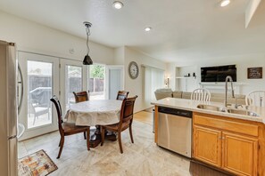 A modern kitchen with a central island, a dining area with a round table and chairs, and a living area with a couch and TV.