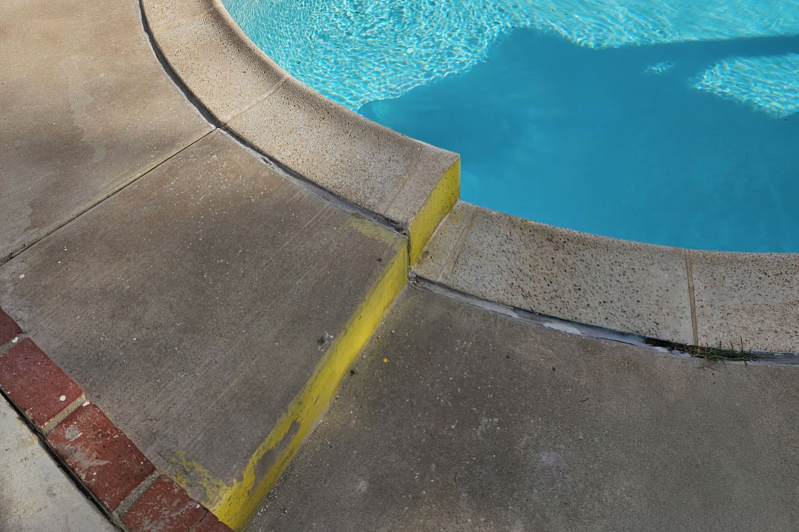 Borde de piscina de hormigón con una línea amarilla que marca el límite.