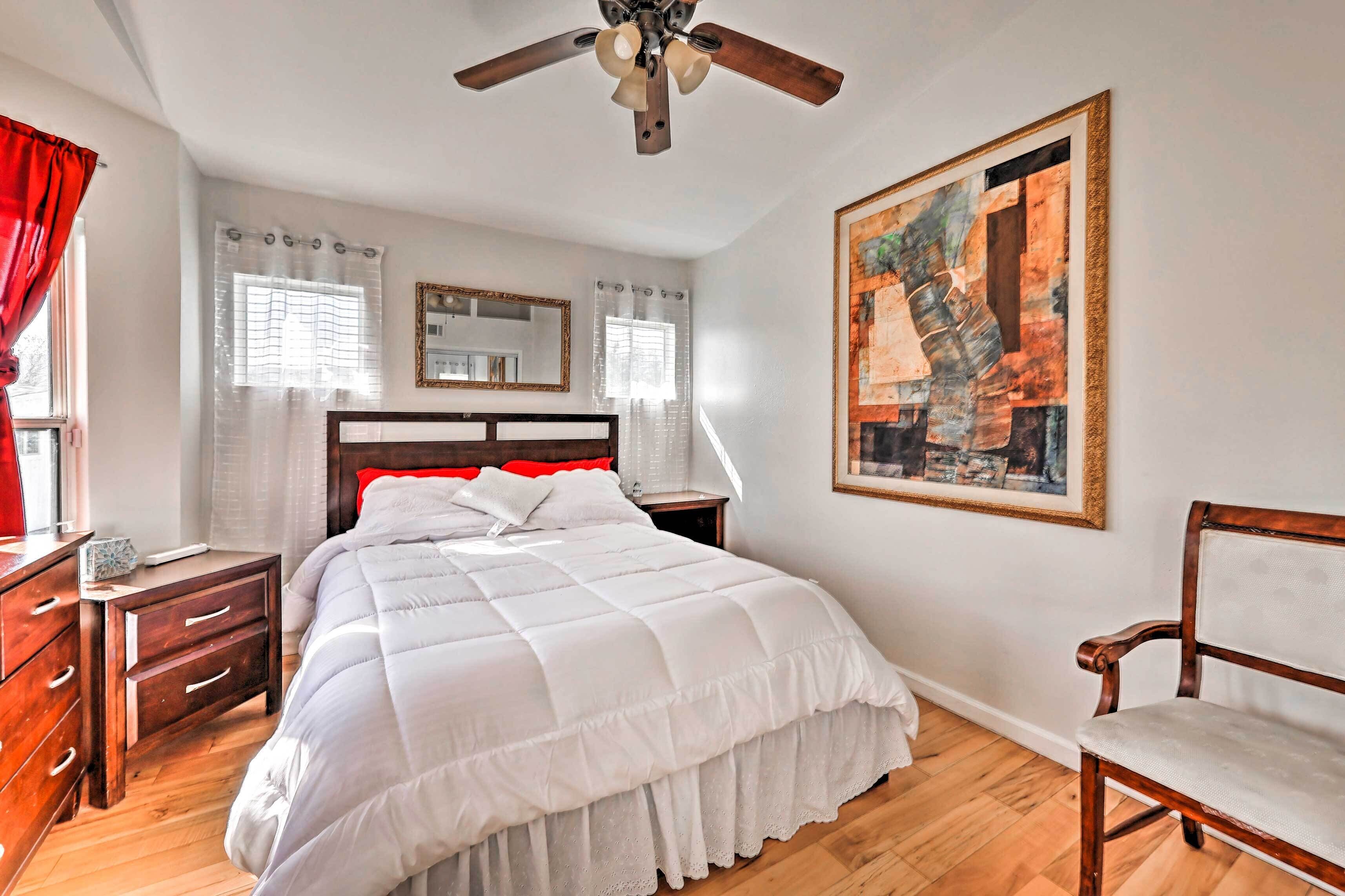 A bedroom with a large bed, wooden nightstands, a ceiling fan, a chair, and artwork on the wall.