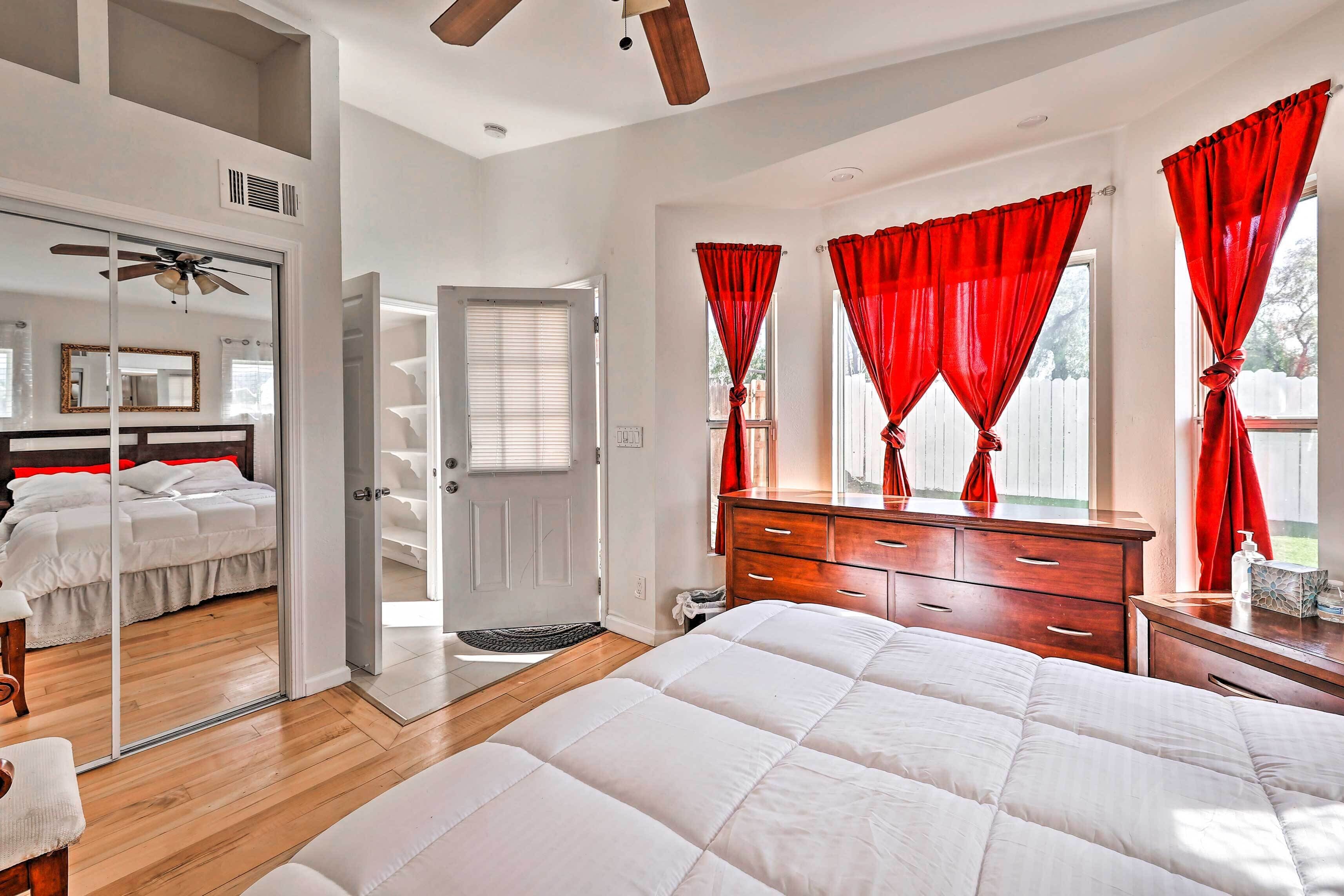 A bedroom with a large bed, a wooden dresser, a mirror, and red curtains.