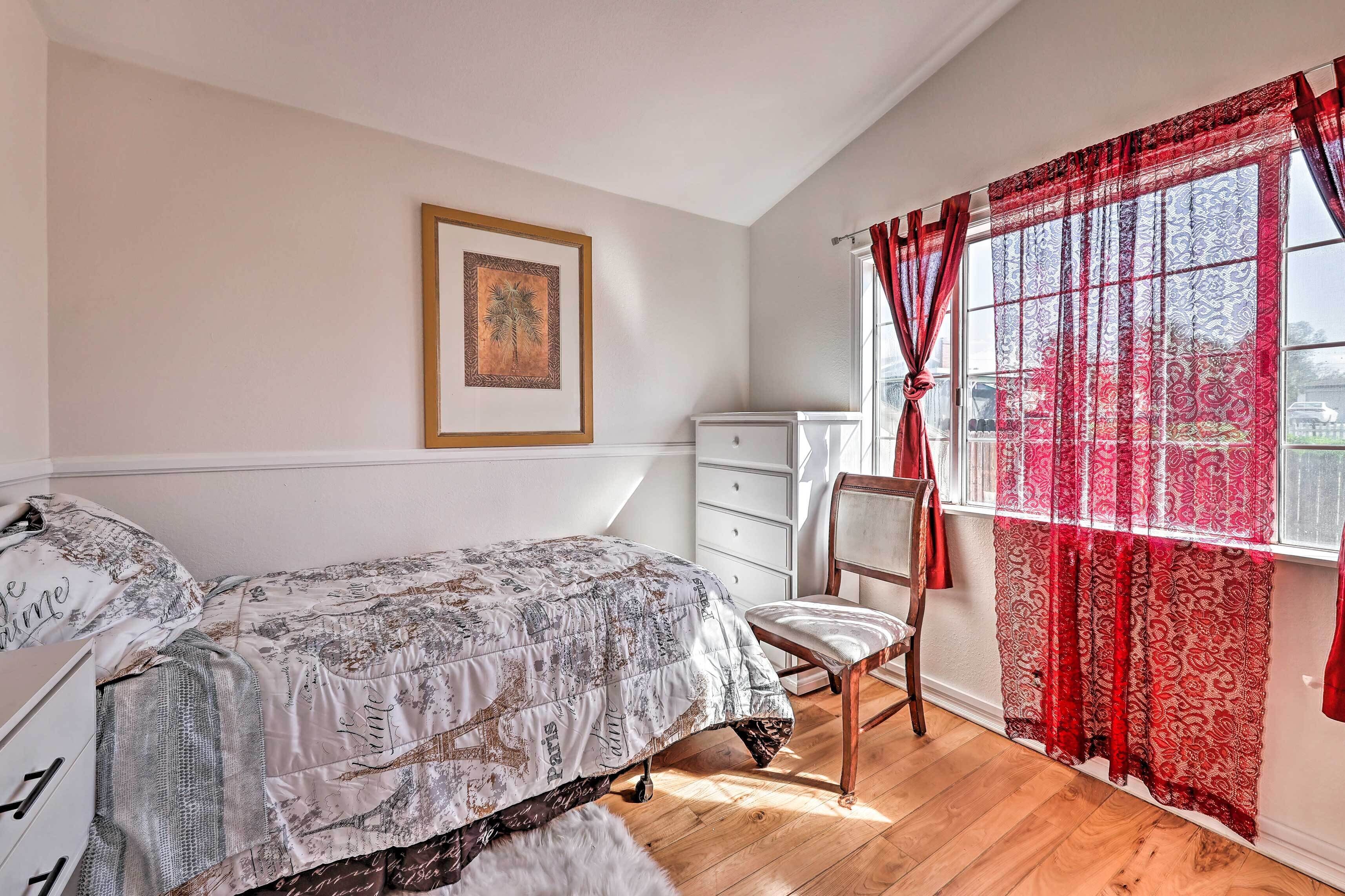 A bedroom with a bed, a chair, a dresser, and a window with red curtains.