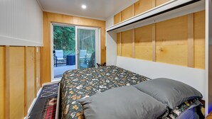 Une chambre à coucher avec un lit, une porte-fenêtre coulissante donnant sur un espace extérieur et une tête de lit en bois.