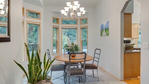 A dining area with a round table, chairs, and a chandelier. There are large windows with multiple panes and a view of greenery outside. - Family-friendly Hot Tub Home in Bonney Lake (Bonney Lake)