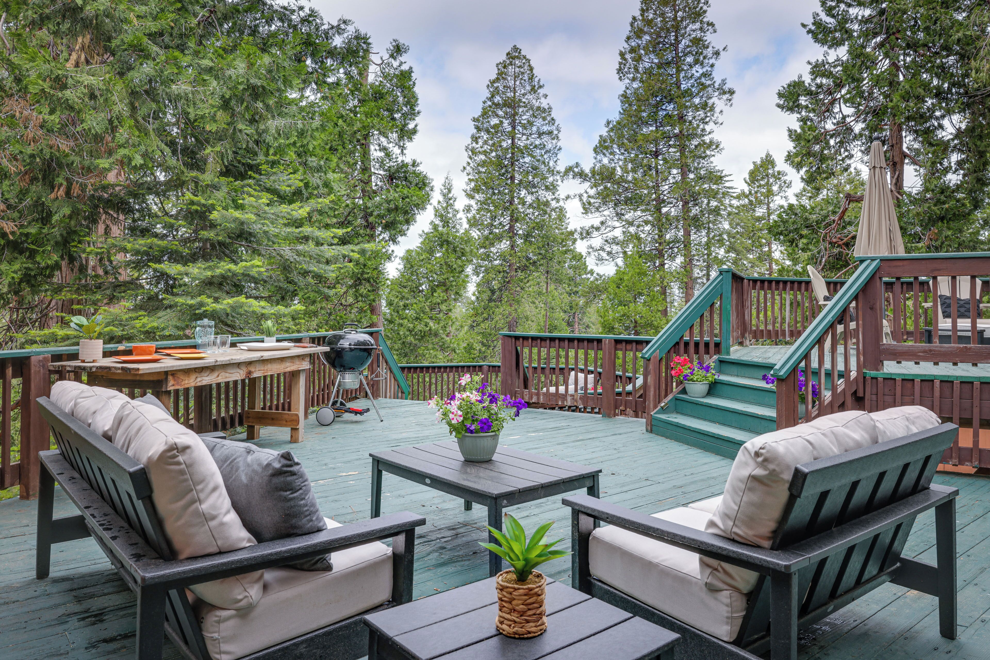 A wooden deck with outdoor furniture, a grill, and a staircase leading to a deck.