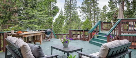 A wooden deck with outdoor furniture, a grill, and a staircase leading to a deck.