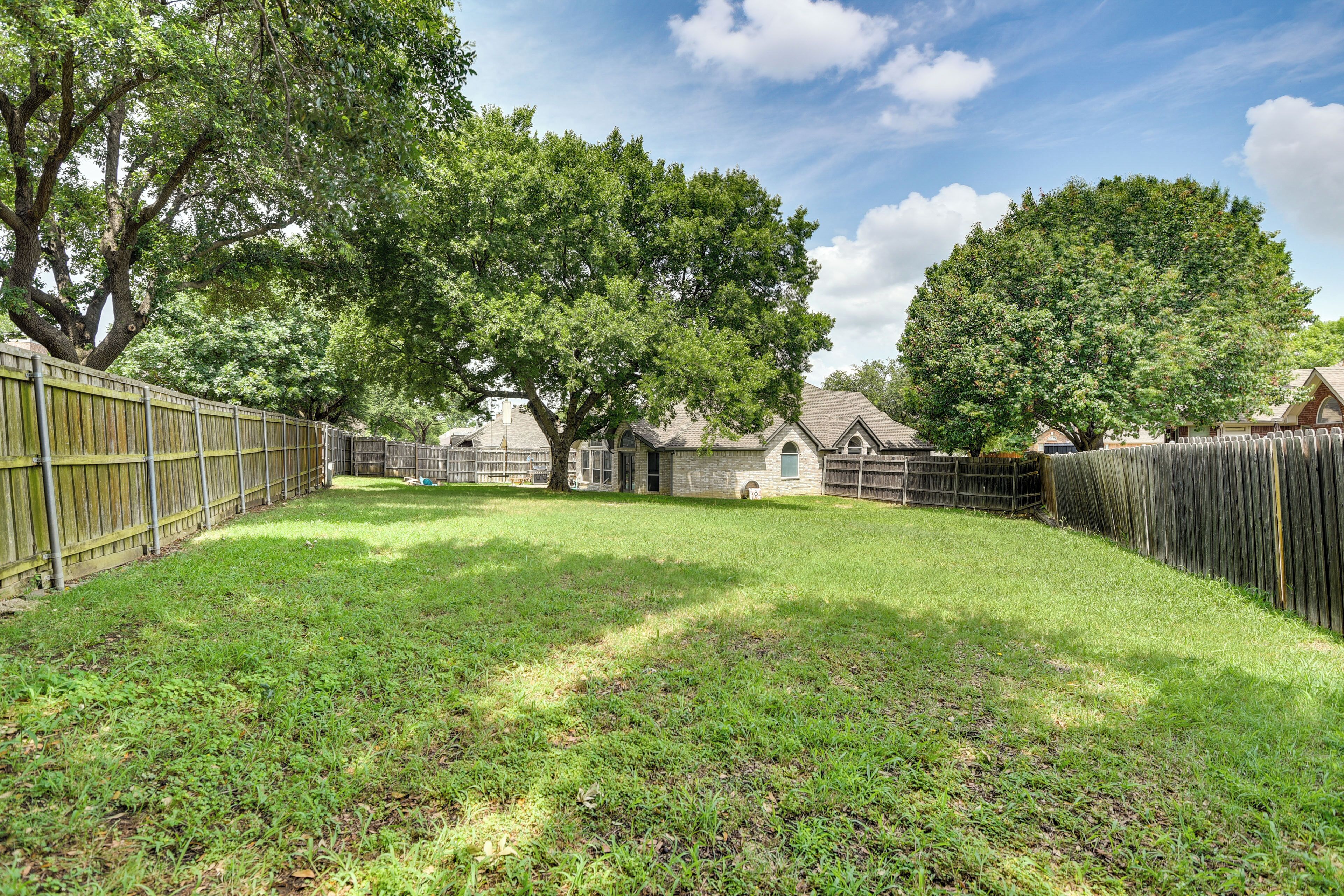A backyard with a wooden fence, a lawn, and a house with a stone chimney.