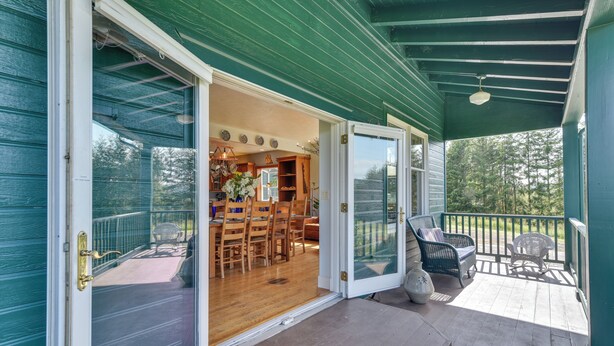 A covered porch with a dining area, a seating area with chairs, and a view of the outdoors. - Rainier Home on 20 Acres w/ Blueberry Farm! (Rainier)
