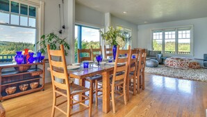 A dining area with wooden chairs and a table set for four, surrounded by large windows with a view of greenery. - Rainier Home on 20 Acres w/ Blueberry Farm! (Rainier)