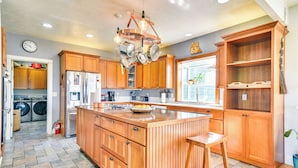 A kitchen with wooden cabinets, a large island, and a hanging pot rack. - Rainier Home on 20 Acres w/ Blueberry Farm! (Rainier)