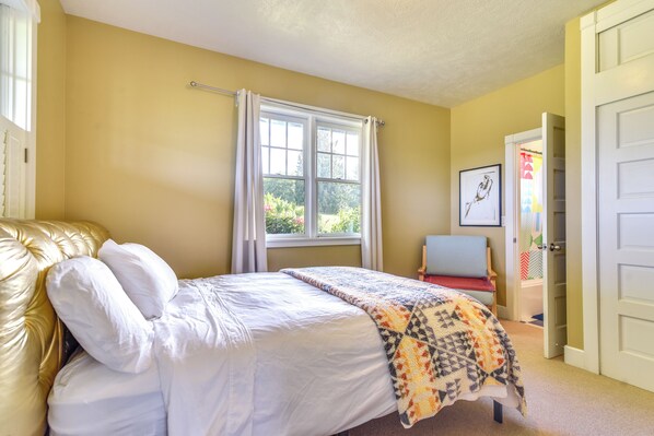 Une chambre à coucher avec un lit, une fenêtre avec des rideaux, une chaise et une porte.