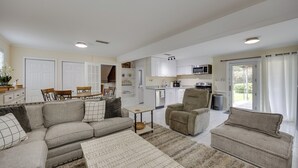 A modern living room with a sectional sofa, armchairs, and a coffee table. A kitchen with white cabinets and appliances is visible in the background. - Mechanicsville Vacation Rental ~ 8 Mi to Richmond (Mechanicsville)