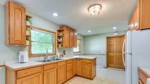 A kitchen with wooden cabinets, a white refrigerator, a sink, and a window with blinds. - Dog-friendly Watertown Vacation Rental w/ Deck (Watertown)