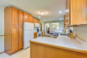A kitchen with wooden cabinets, a refrigerator, a microwave, and a dining area with a table and chairs. - Dog-friendly Watertown Vacation Rental w/ Deck (Watertown)