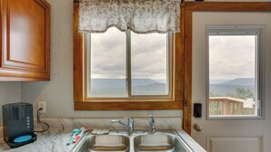 A kitchen with a double sink, a coffee maker, and a window with a view of mountains.