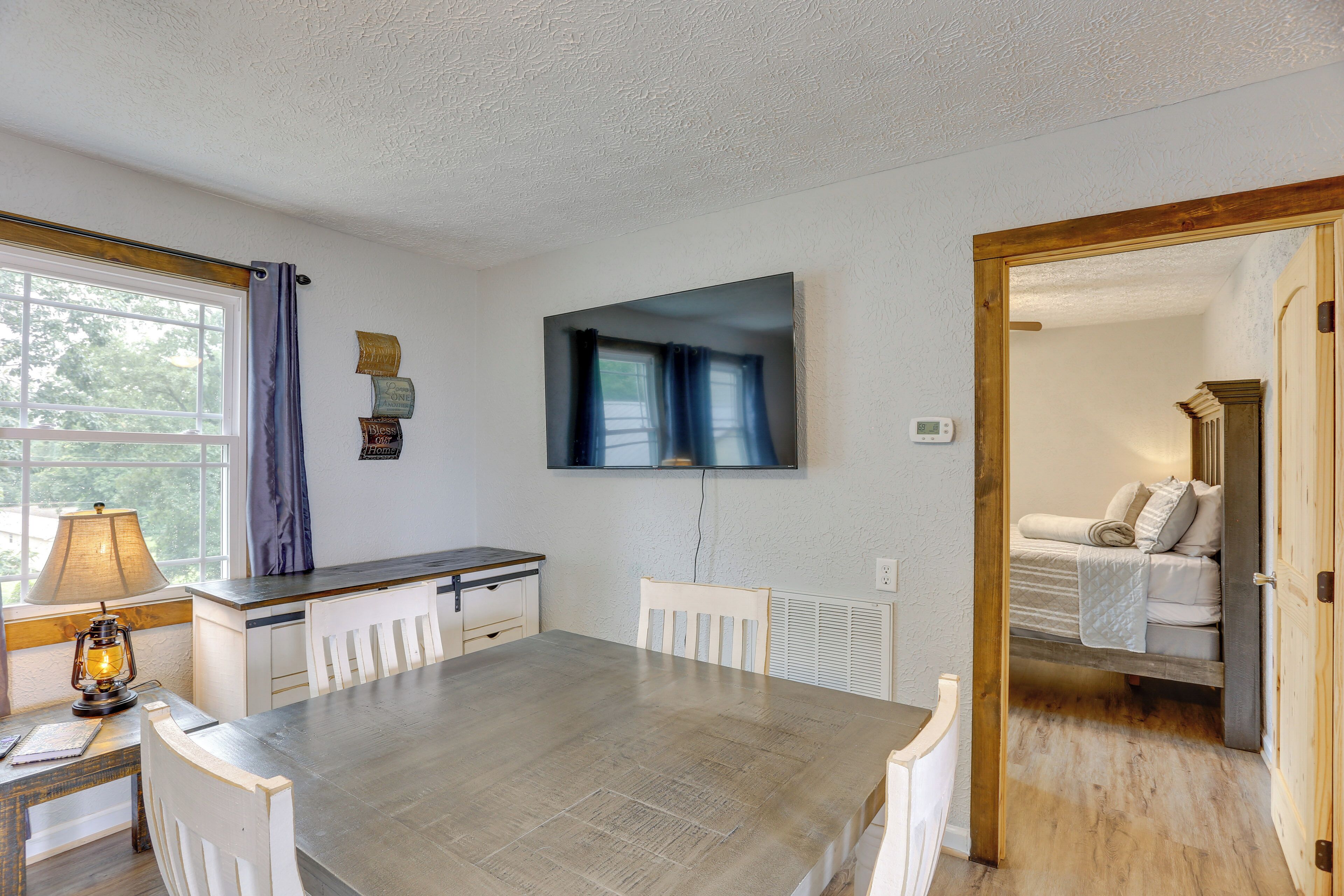 Un coin repas avec une table en bois, des chaises blanches, une lampe et une fenêtre avec des rideaux.