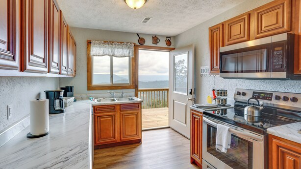 A kitchen with wooden cabinets, a stainless steel microwave, a stove, and a large window offering a view of the outdoors.